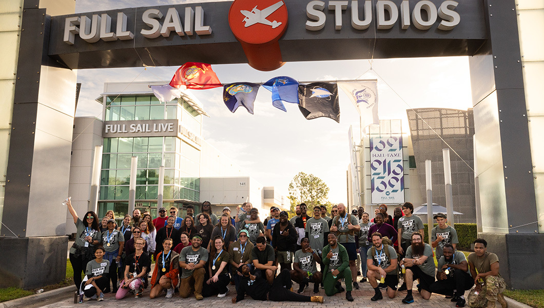 Dozens of student veterans gather under the Full Sail Studios sign in front of the Full Sail Live venue at sunset.