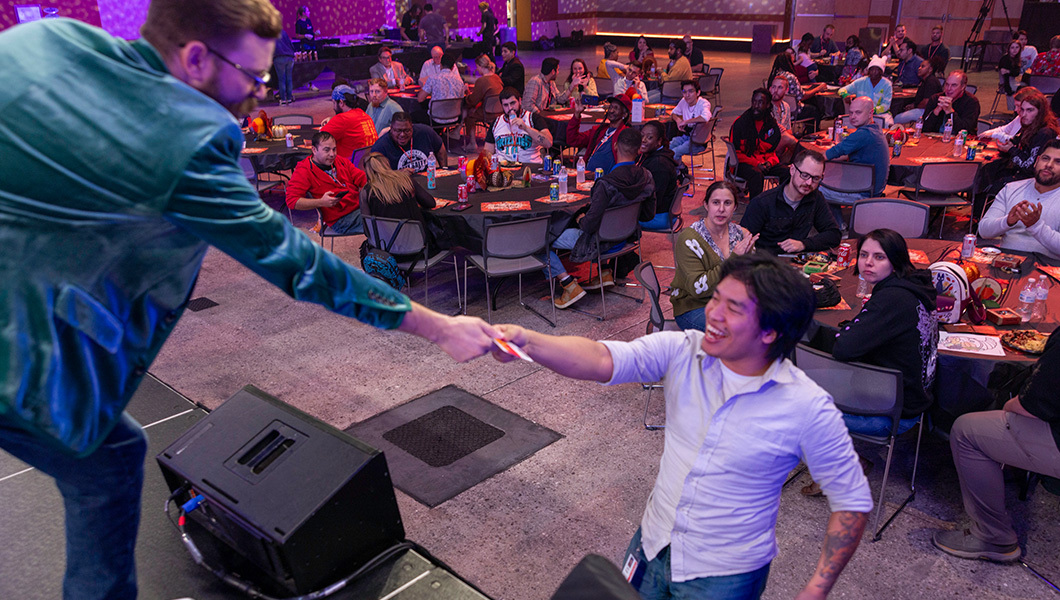 A smiling student hands their raffle ticket to an event organizer. Veteran students and families sit at tables in the background.