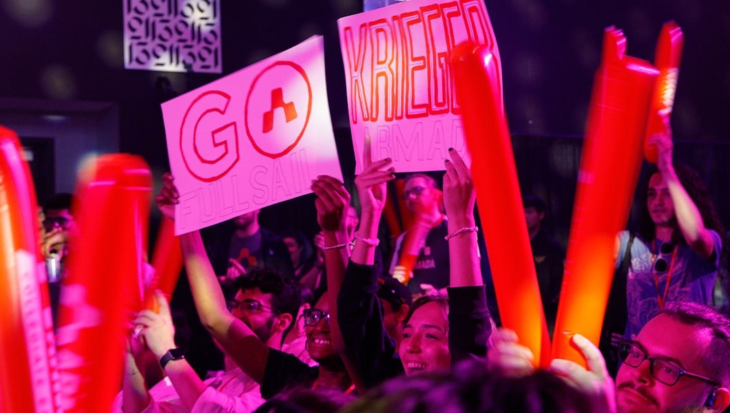 A crowd of people waving orange thunder sticks with the Armada logo and signs that read “Go Krieger”.