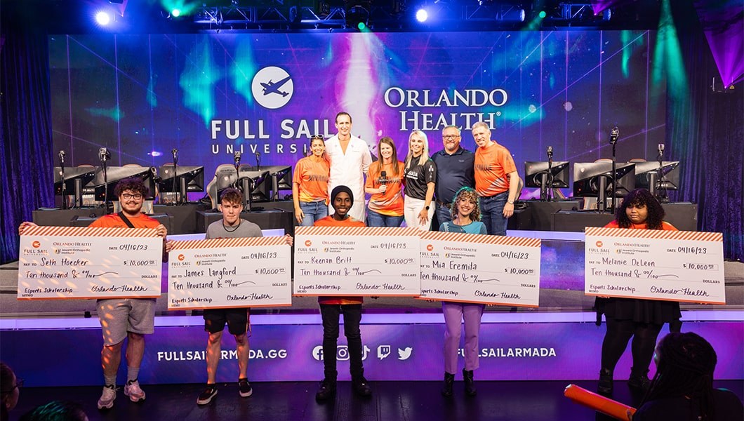 Full Sail staff and OrlandoHealth representatives on stage posing for photos with five students holding large scholarship checks.