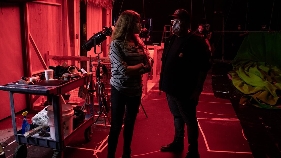 A man and a woman stand next to each other surrounded by cameras and film equipment on a sound stage