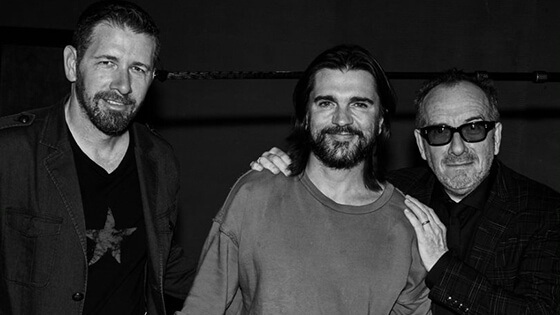 Sebastian stands next to Juanes and Elvis Costello. Sebastian wears a t-shirt and jacket, Juanes wears a t-shirt, Elvis wears a jacket.