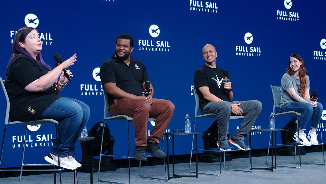 Speakers seated on stage in front of a large blue LED screen featuring the Full Sail logo repeating.