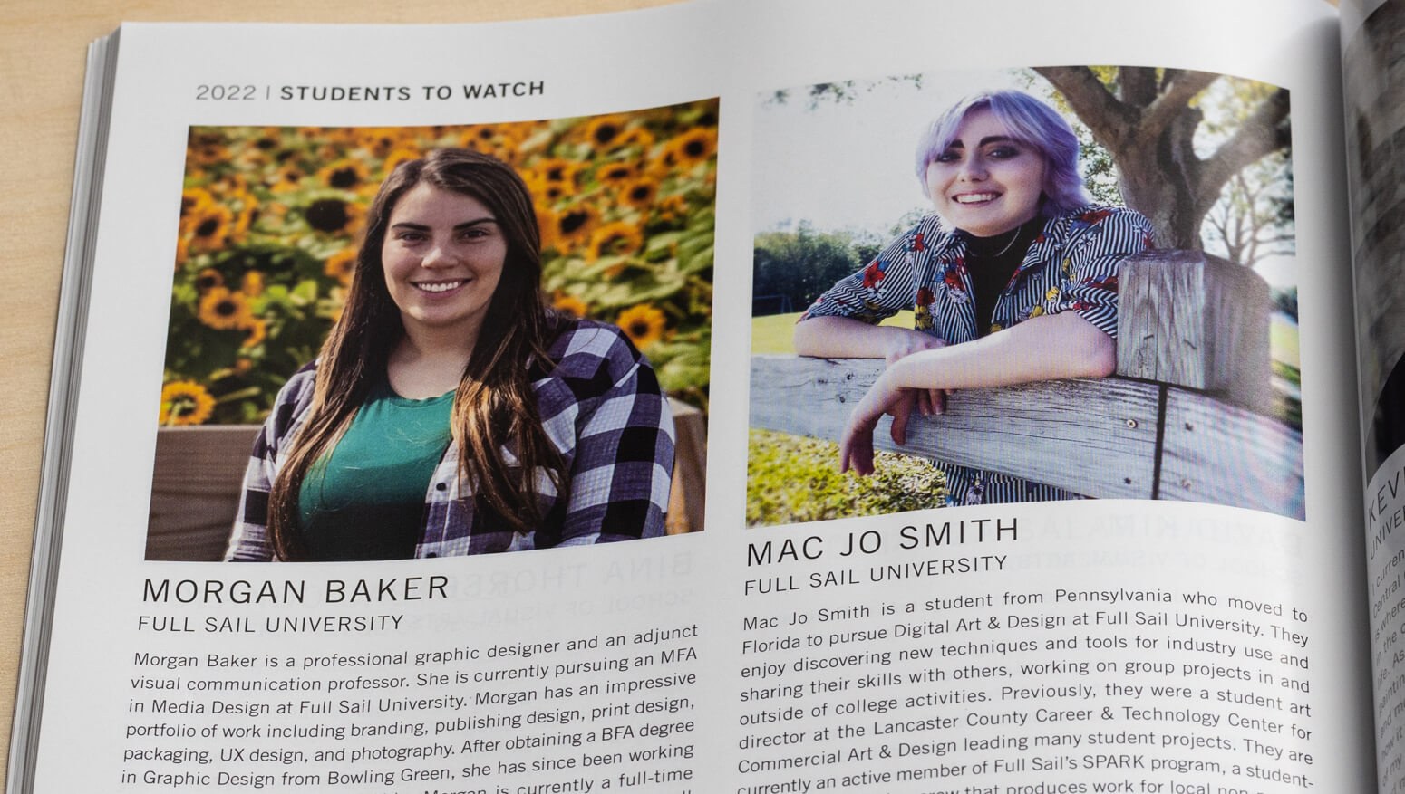 A Graphic Design USA magazine is open to a page featuring two smiling Full Sail students, Morgan Baker and Mac Jo Smith. Morgan Baker has long brown hair and sits on a bench in front of a wall of sunflowers. Sporting a purple do, Mac Jo Smith leans casually over a wooden fence.