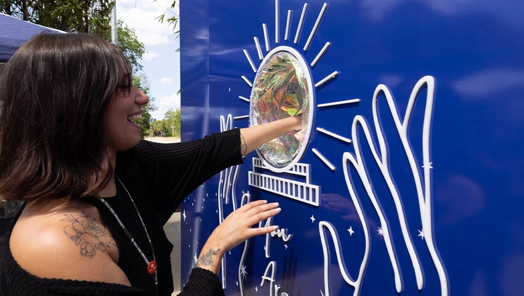 A woman is reaching into a holographic circle on a wall that reads “Dear Future Me” and “You Are Magic.” She is smiling and wearing all black.