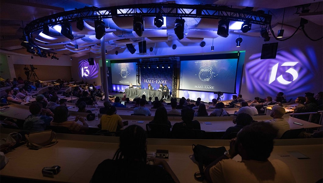 The panelists and moderator, Brandy Price, sit at a table in an auditorium. Brandy is speaking and the panelists are looking in her direction.