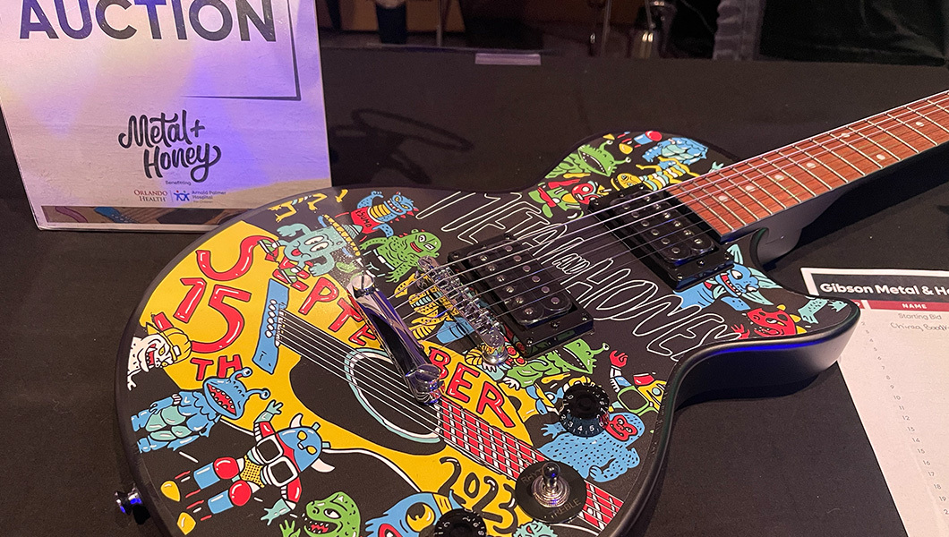 The body of a black electric guitar with a colorful graphic appliqué next to a sign that reads “silent auction.”