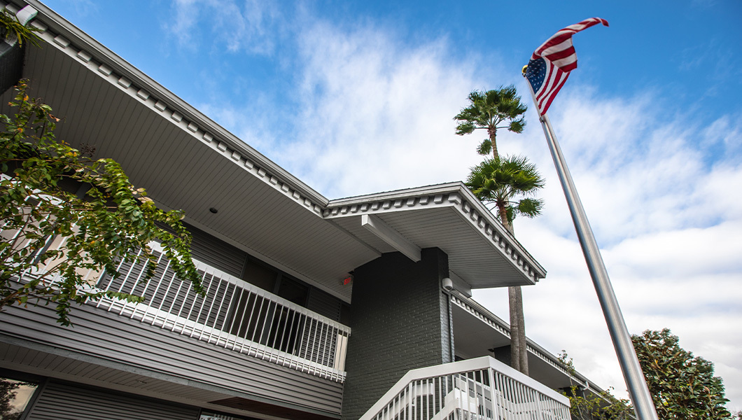 An exterior view of Full Sail’s Military Student Success Center, featuring a U.S. flag and palm trees against a blue sky.
