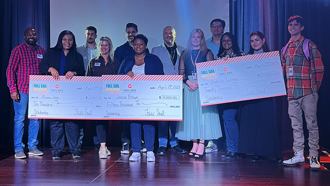 The finalists, participating faculty, and judges stand together. The three winners are holding over-sized checks. Everyone is smiling.