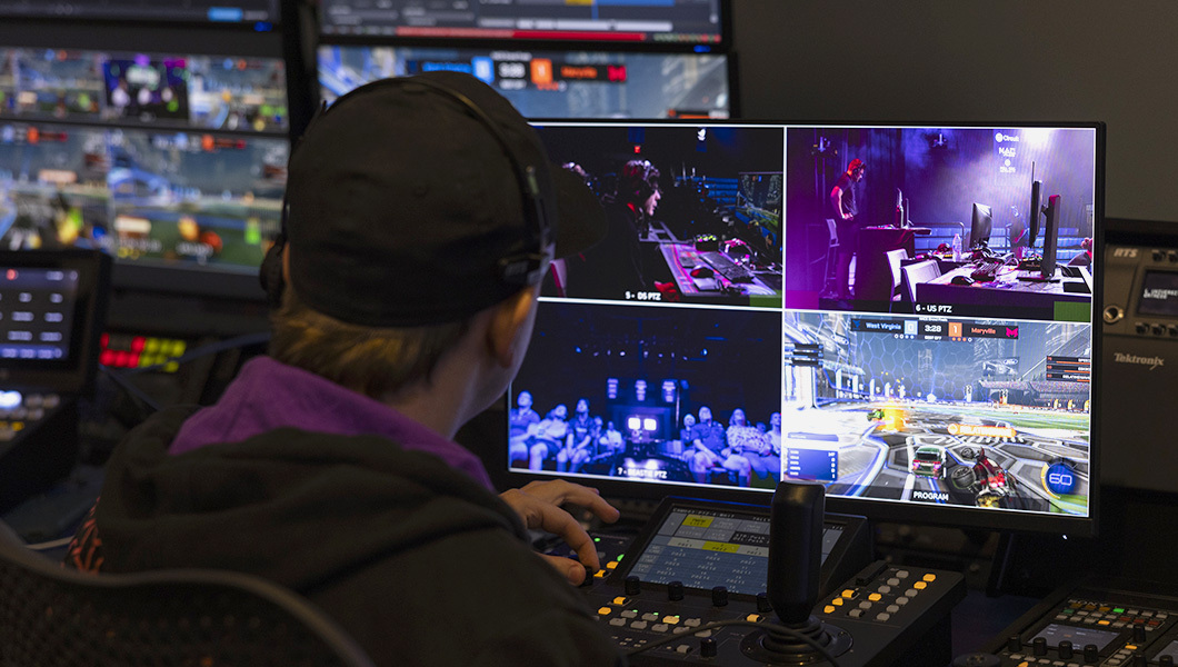 A member of the Full Sail Armada Production Crew sits at a broadcast console and works on a computer screen split into four views of an esports tournament.