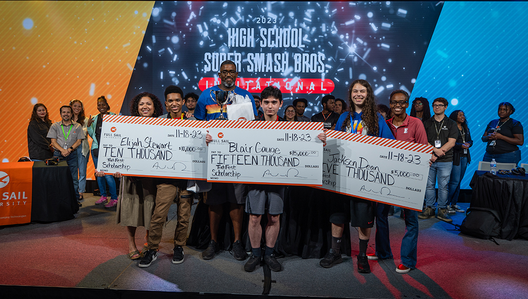 Three young people are seen on stage holding large novelty checks with scholarship funds from Full Sail.