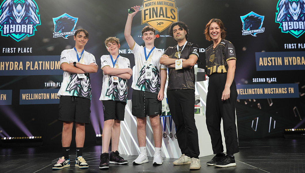 Three esports players and their coach are on stage accepting an award, the player in the middle is holding the award overheard.
