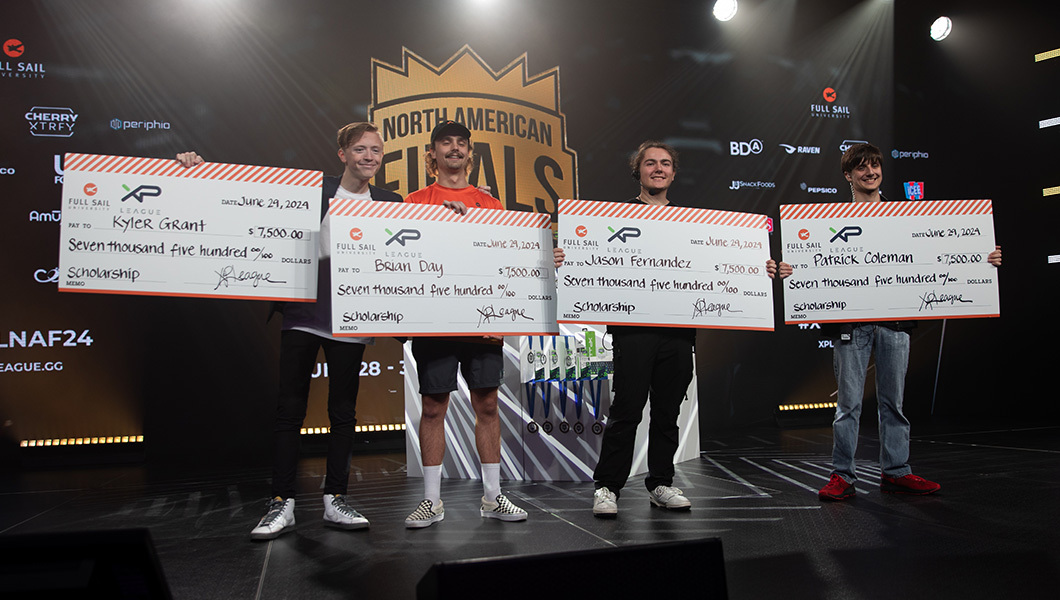 Four students pose for a picture together on stage while holding oversized checks awarding scholarship funds.