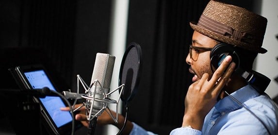 An Audio Production student speaks into a recording microphone while reading a script from an iPod.