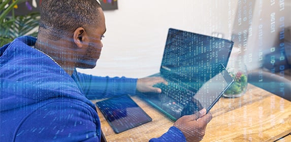 A woman with glasses in a tech setting looking at several monitors with code.