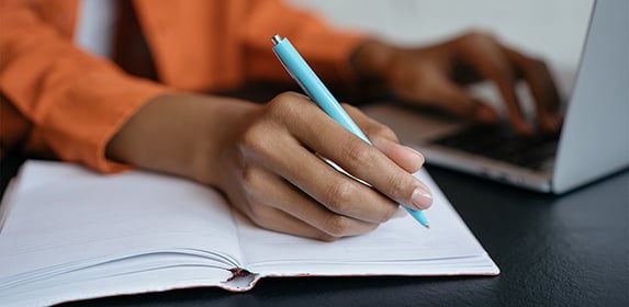 A student uses a laptop and writes in a notebook.