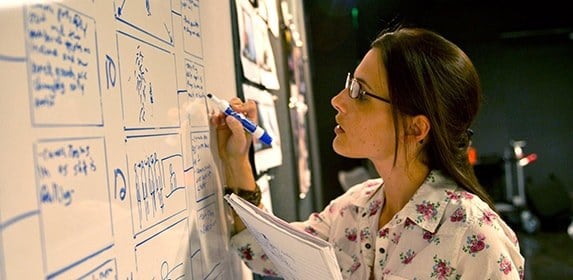 A student writes storyboard notes on a whiteboard.