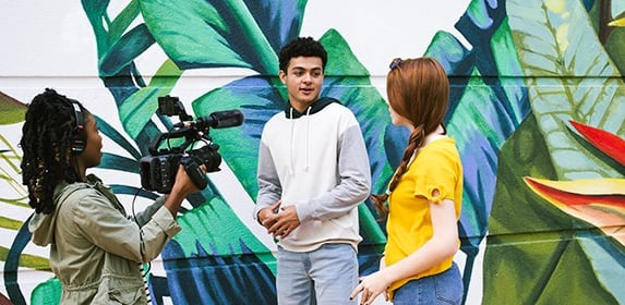 A crew of three Digital Cinematography students prepares their camera and audio equipment for an upcoming shot for a film.