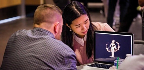 Two students look at a 3D model of a pixelated person.