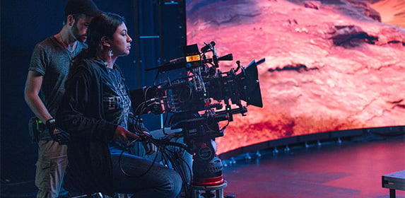 Film Production students film an actor exiting a car during a scene using a studio-quality Sony video camera.