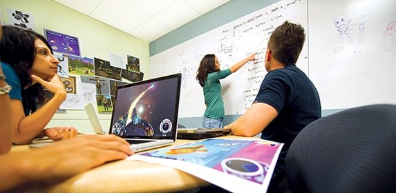 Three students use a live science-fiction game demo to plan out art arrangements within the project’s code.