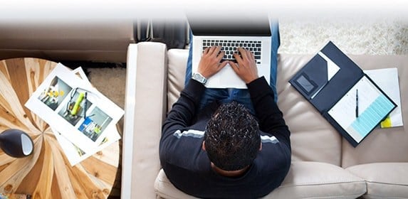 A student works on a laptop with written notes and printed mockups next to them.