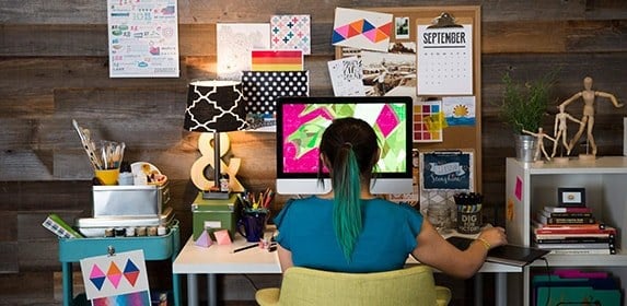 A student surrounded by colorful accessories, reference books, and art tools creates a green, geometric reptile.