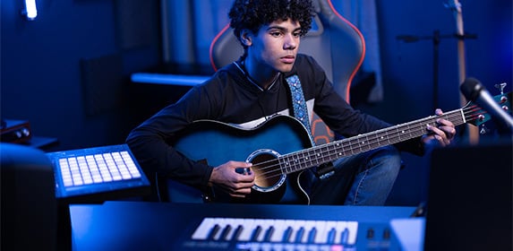 A Music Production student plays a guitar in a recording studio.