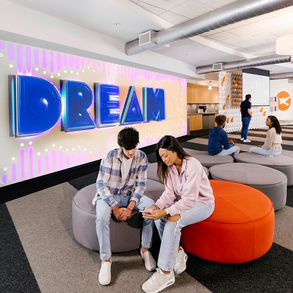 Two students sit in front of the Full Sail dream wall.