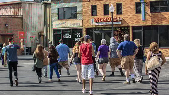 A group of smiling students walks under the Full Sail Studios arch on Full Sail’s campus. The Full Sail Live venue is behind the arch.