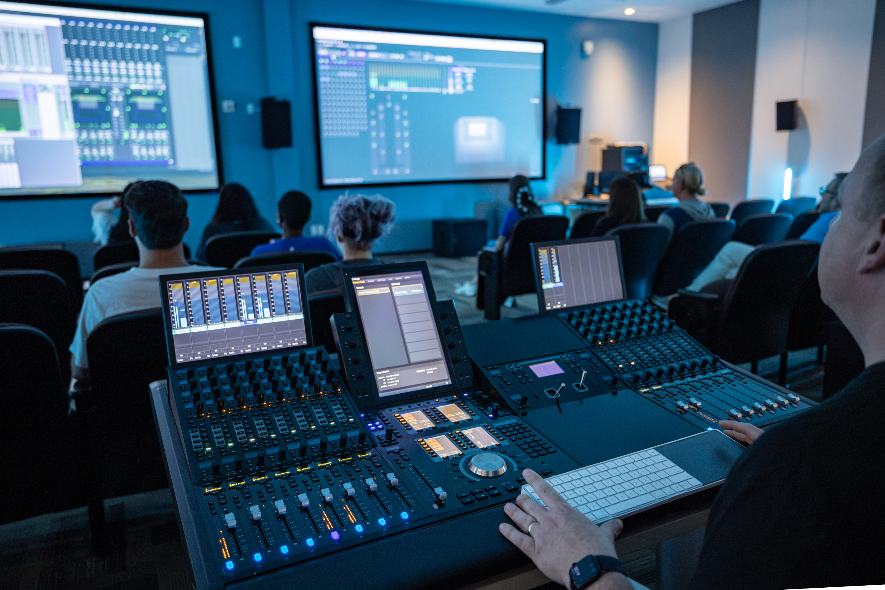 Photograph inside the Atmos classroom with an instructor behind an Avid console and the audio settings are projected for students in the classroom to see.