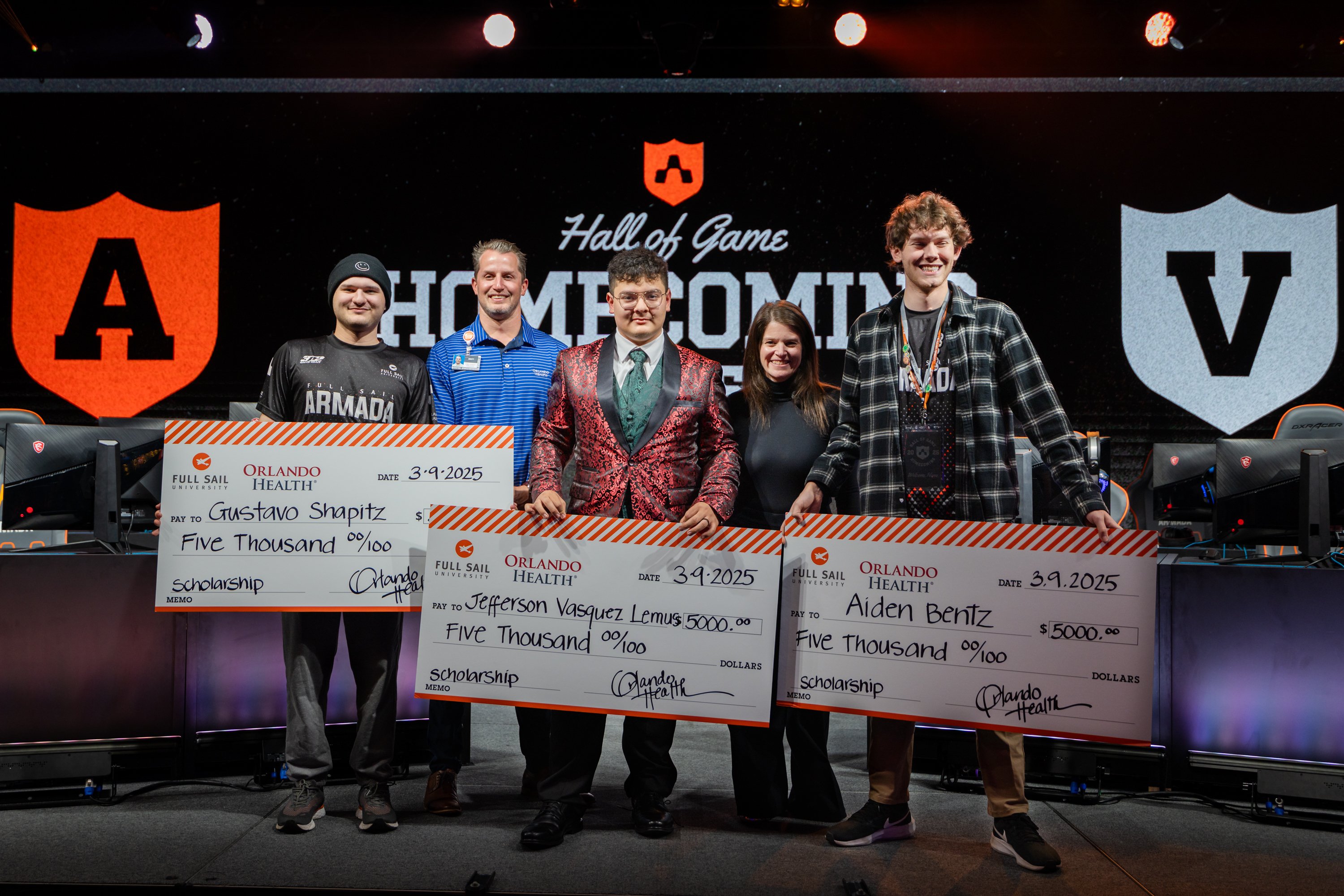 Five people on stage with three people holding large $5,000 checks.