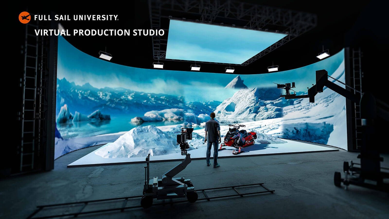 A man wearing jeans, sneakers, and a plaid shirt stands in a production studio. He is facing a large LED screen showing an icy mountain range and a snowmobile.