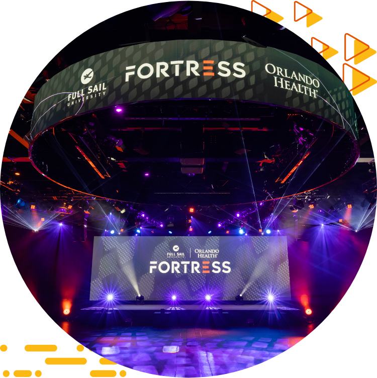 A photograph of the Full Sail Orlando Health Fortress, with spotlights and multiple display screens containing logos for the esports space.