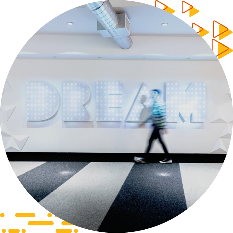 Large white wall with the word DREAM on it; in the foreground, a blurry outline of a male student walking past.